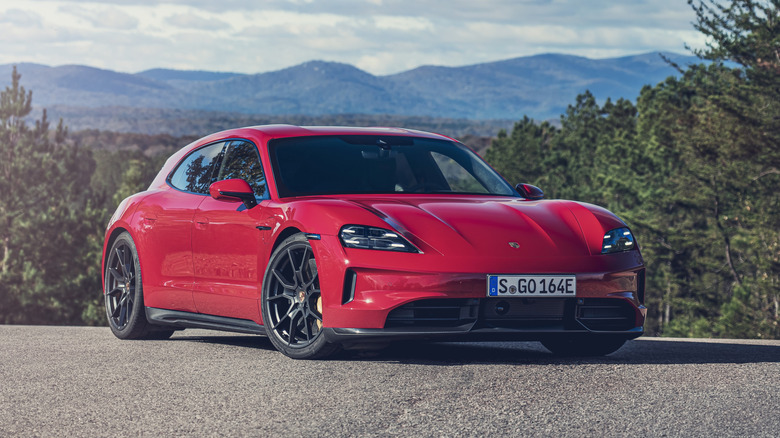나무와 산을 배경으로 아스팔트 위에 주차된 빨간색 Porsche Taycan