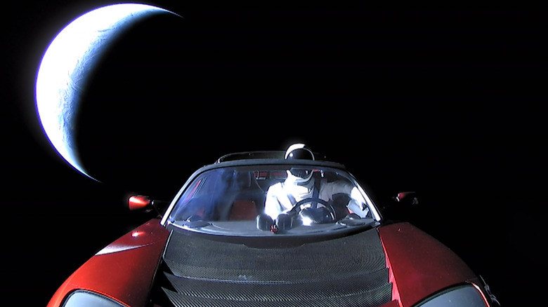 뒤에 지구가 있는 우주에 빨간색 Tesla 로드스터가 있습니다.