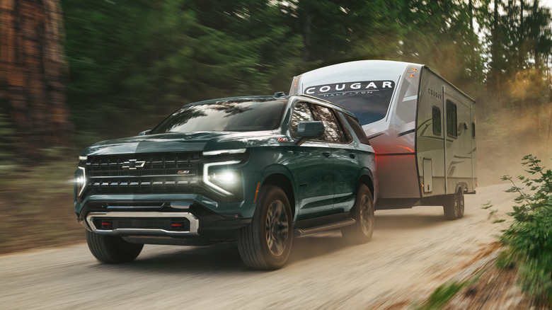비포장 도로를 따라 트레일러를 견인하는 녹색 2026 Chevy Tahoe의 전면 3/4 모습.