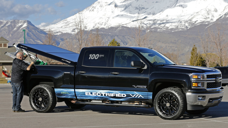 검정색 Chevy Silverado 픽업 트럭에서 태양열 토너 커버를 들어올리는 남자의 모습.