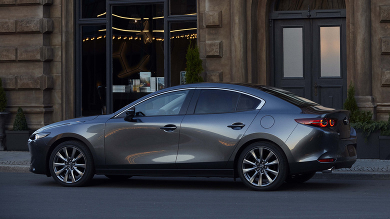 웅장한 빅토리아 시대 건물 앞에 주차된 회색 Mazda3 세단.