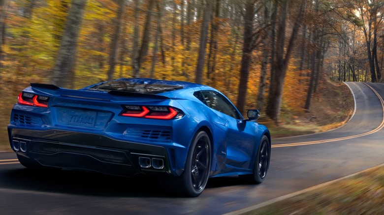 숲이 우거진 2차선 도로를 주행하는 파란색 2026 Chevrolet Corvette E-Ray의 후면 모습