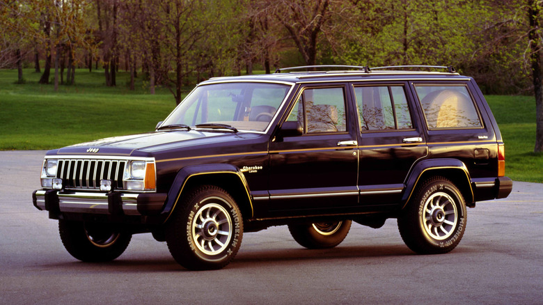 숲 앞 주차장에 주차된 1985 Jeep Cherokee XJ, 전면 왼쪽 3/4 뷰