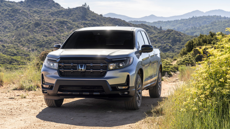 흙길을 달리는 은색 2026 Honda Ridgeline, 배경에는 산