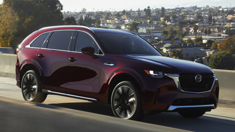 교외 환경의 고속도로 진입로에 있는 Mazda CX-90의 전면 3/4 뷰
