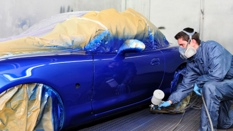 전문 페인트 부스에서 Mazda MX-5에 파란색 페인트를 뿌리는 자동차 기술자