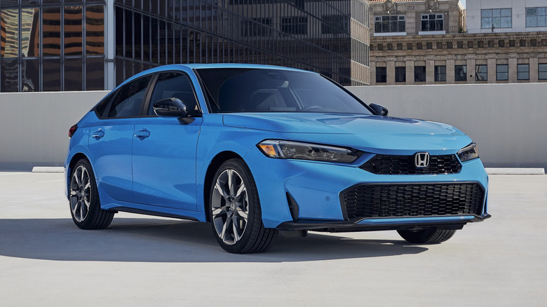 도시의 주차장 위에 주차된 파란색 2026 Honda Civic Sport Touring 하이브리드 해치백