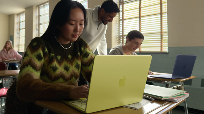 교실 책상 위에 노란색 MacBook Neo를 사용하고 있는 사람과 그 뒤에 다른 사람들이 있습니다.