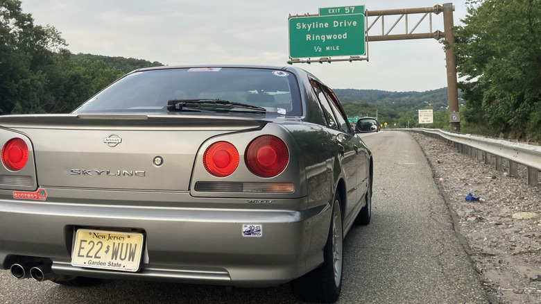 2000 Nissan Skyline R34가 출구 표지판을 읽고 고속도로 옆에 주차되어 있습니다. 