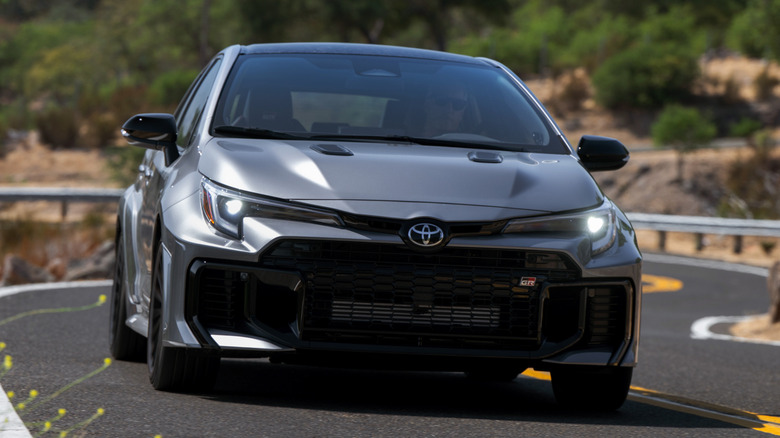 숲이 우거진 지역의 구불구불한 도로에 있는 2026 Toyota GR Corolla의 전면 모습