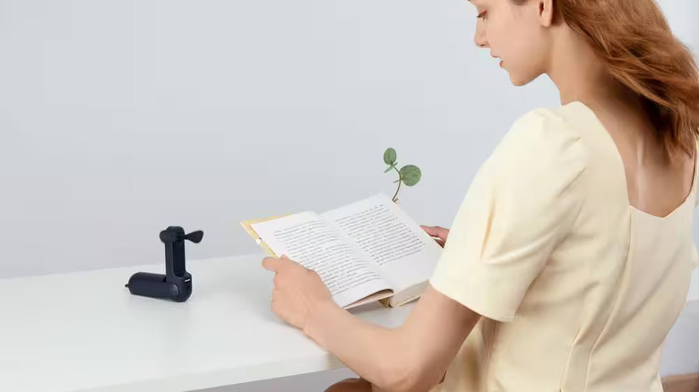 책을 읽고 있는 여성을 식혀주는 홈디포 휴대용 선풍기.