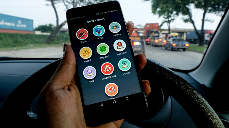 차 안에서 Waze로 신고 화면 보내기를 보여주는 스마트폰을 들고 있는 사람