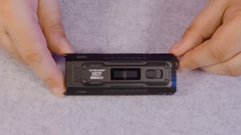 회색 배경에 Nitecore EDC37 손전등을 들고 있는 손의 하향식.