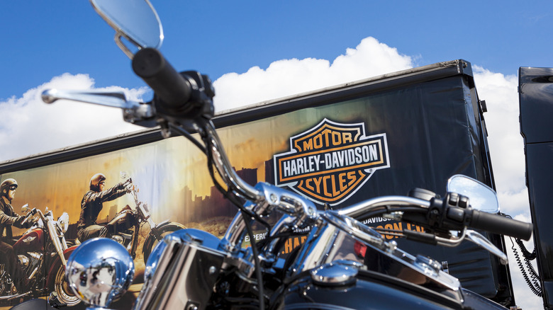 Harley-Davison 트럭을 배경으로 크루저 오토바이 핸들바를 클로즈업합니다.