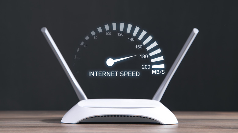 나무 테이블 위에 두 개의 안테나가 있는 Wi-Fi 라우터와 그 위에 인터넷 속도를 나타내는 속도계 그래픽이 있습니다.