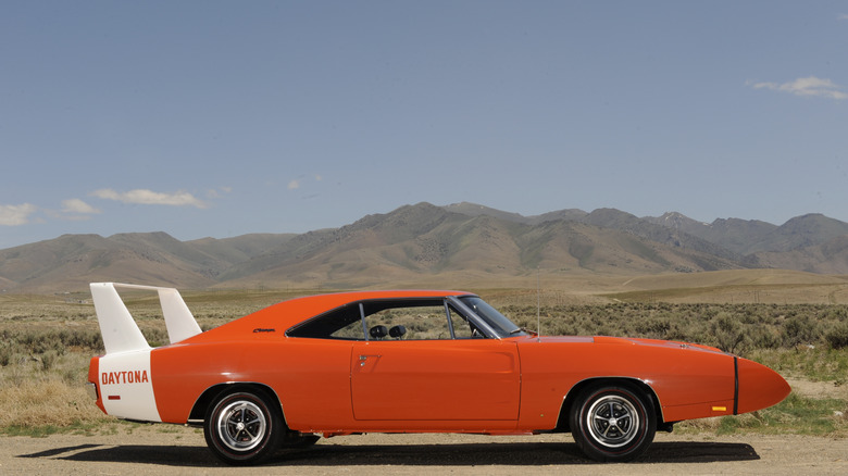 주황색 1969년형 Dodge Charger Daytona Nascar 경주용 자동차가 노즈콘과 흰색 날개를 갖춘 흙 표면 위에 서 있습니다.