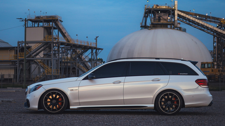 산업 지역에 주차된 흰색 메르세데스 E63 AMG 왜건의 측면 전망.