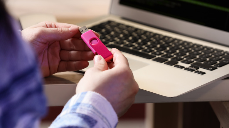 분홍색 USB 플래시 드라이브를 들고 노트북 앞에 앉아 있는 여성의 사진