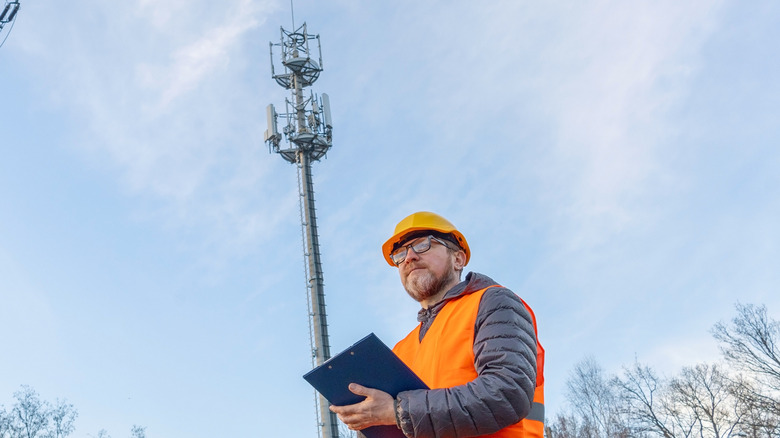 5G 타워를 배경으로 클립보드를 들고 서 있는 작업자