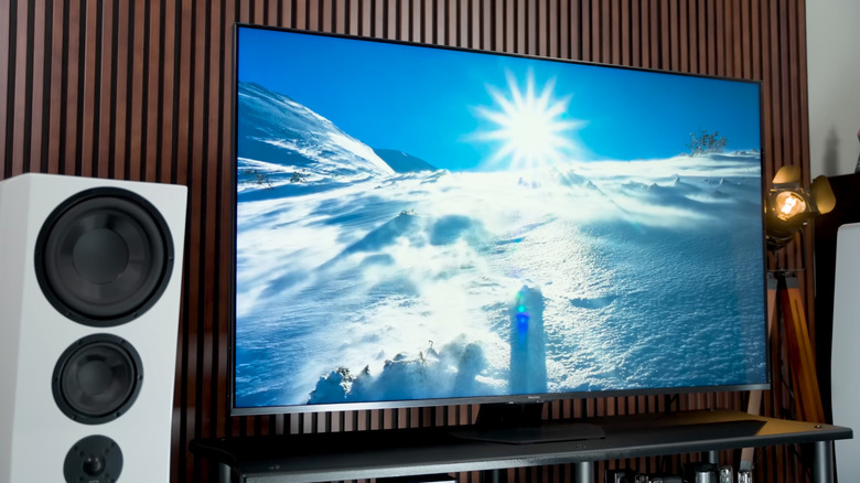눈 덮인 산의 풍경을 보여주는 Hisense U8QG TV와 그 옆에 있는 흰색 홈 시어터 스피커