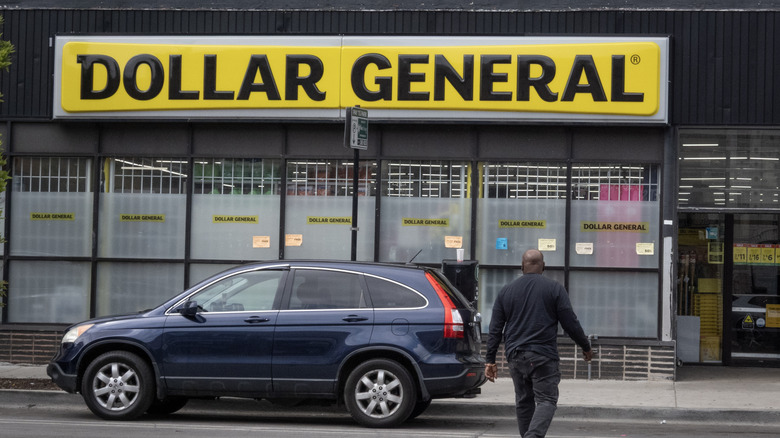 달러 제너럴(Dollar General) 밖에 주차된 자동차와 정문으로 걸어가는 사람.