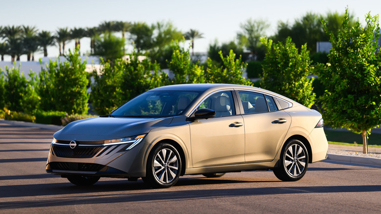 나무줄기를 배경으로 포장도로에 주차된 금색 2027 Nissan Sentra