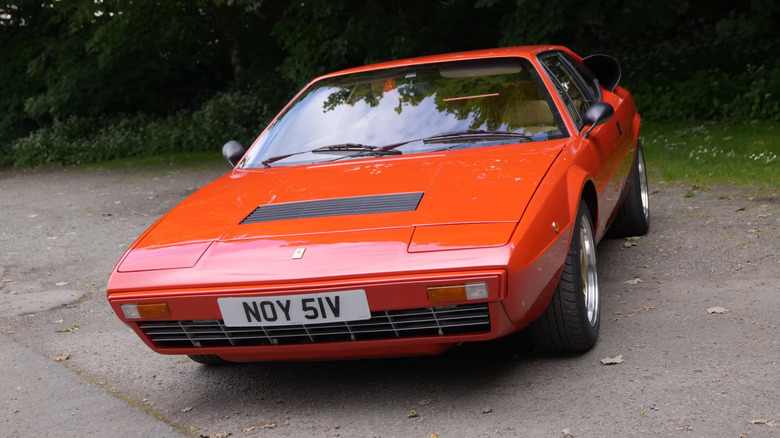 클래식한 빨간색 페라리 페인트로 마감된 1980년형 Ferrari Dino 308 GT4가 길가에 비스듬히 주차되어 있습니다.