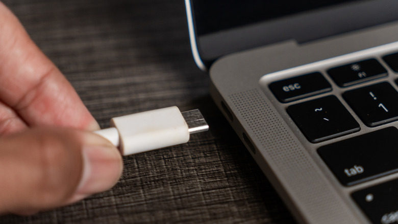 흰색 USB-C 케이블을 노트북에 연결하는 손 클로즈업