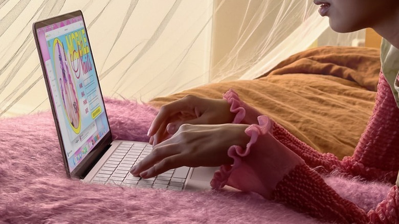 침대 위에서 MacBook Neo에 타이핑을 하고 있는 손