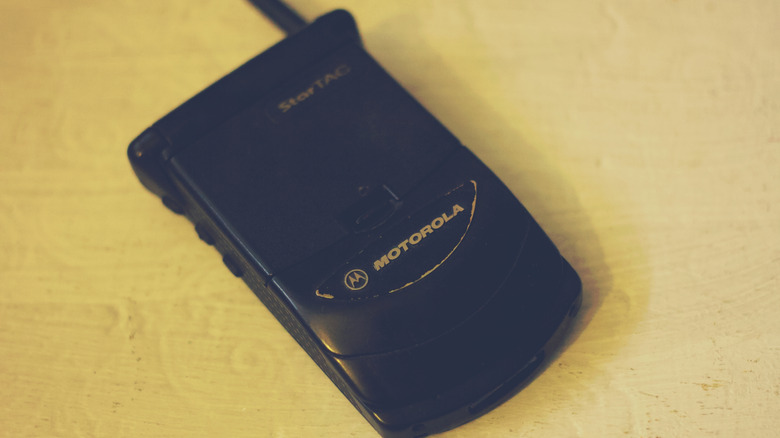 나무 표면에 닫혀 있는 검은색 Motorola StarTAC 플립 휴대폰