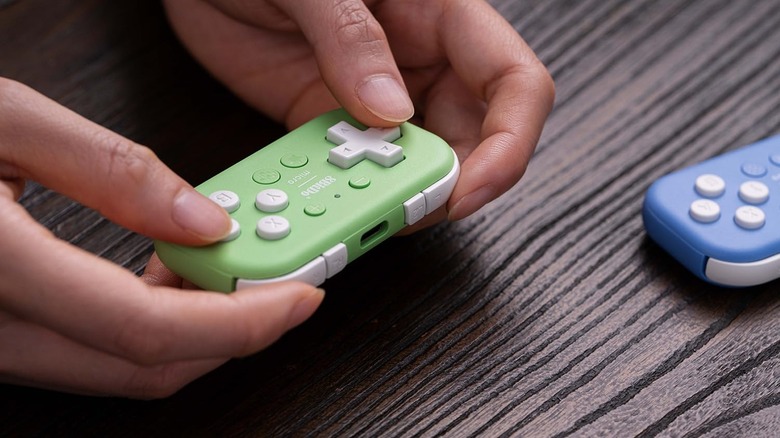 8BitDo Micro 컨트롤러를 들고 있는 사람과 다른 사람이 근처에 있습니다.