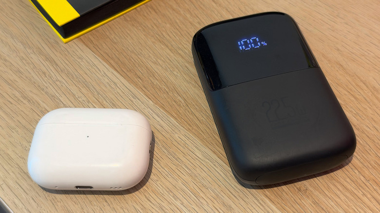 나무 테이블 위의 AirPods 케이스 옆에 보조 배터리가 있습니다.