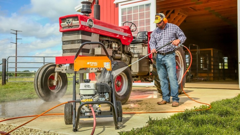 헛간 앞의 트랙터를 청소하기 위해 Stihl RB 400 Dirt Boss 고압 세척기를 사용하는 남자
